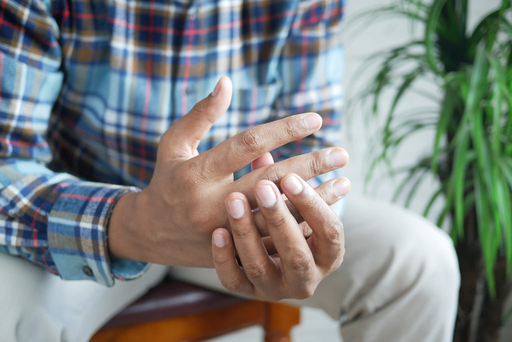 An elderly man clutching his own hand tightly, his grip reflecting the pain he feels in his joints.