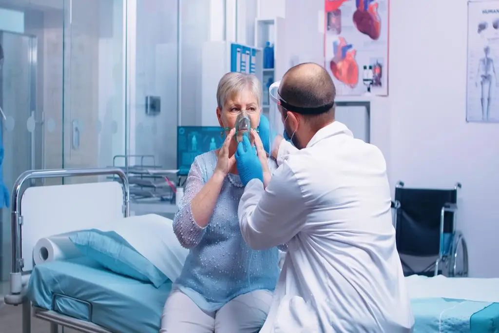 Doctor putting an oxygen mask on retired senior woman in modern private hospital or clinic.