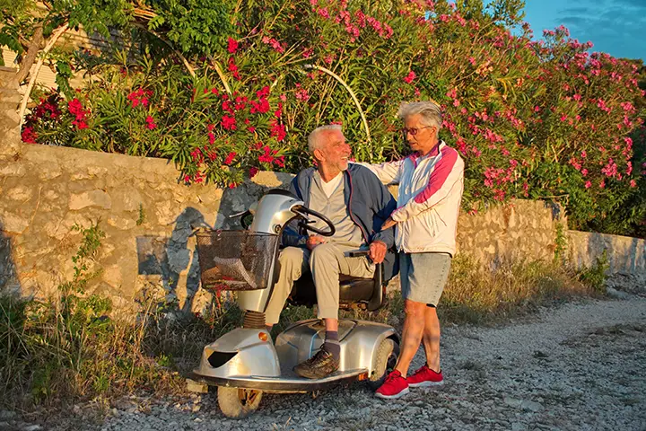 Senior couple walking along promenade by the Adriatic sea - disabled man riding scooter