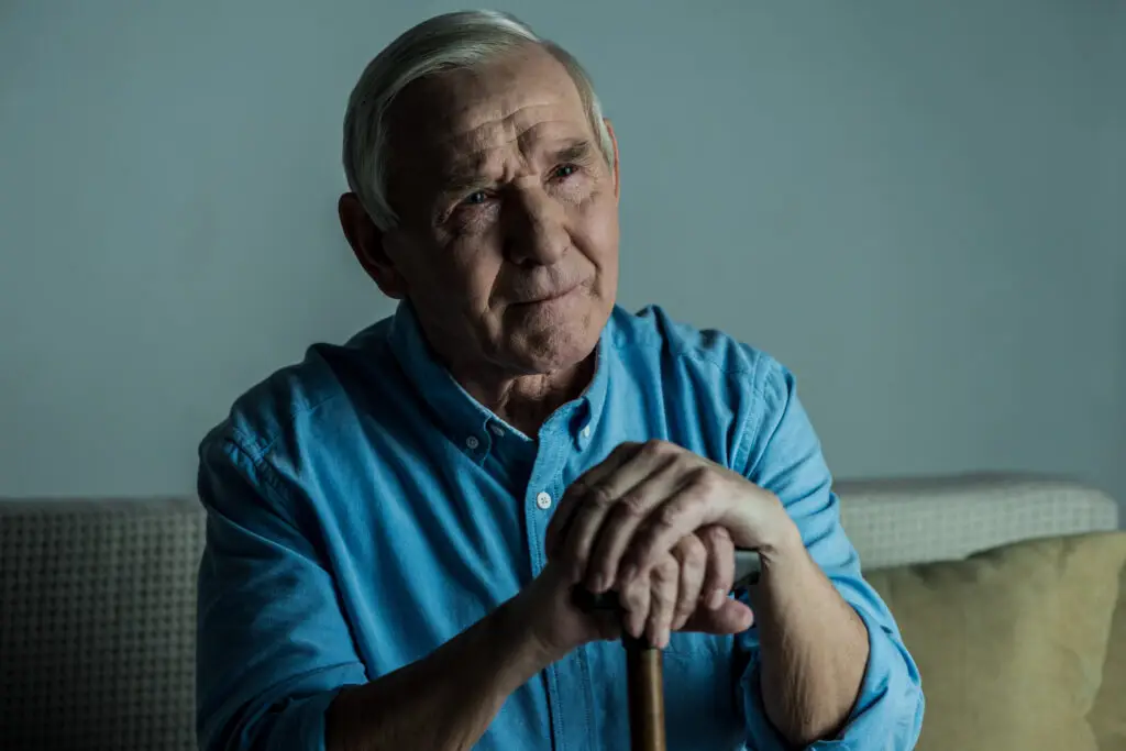 Senior man leans on a cane while sitting on sofa in contemplation