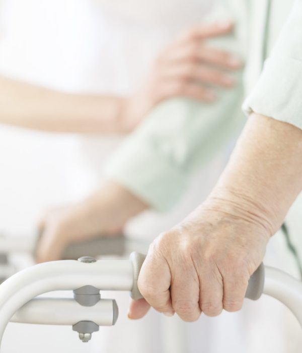 Nurse in white uniform supporting elderly person using a walker at nursing home